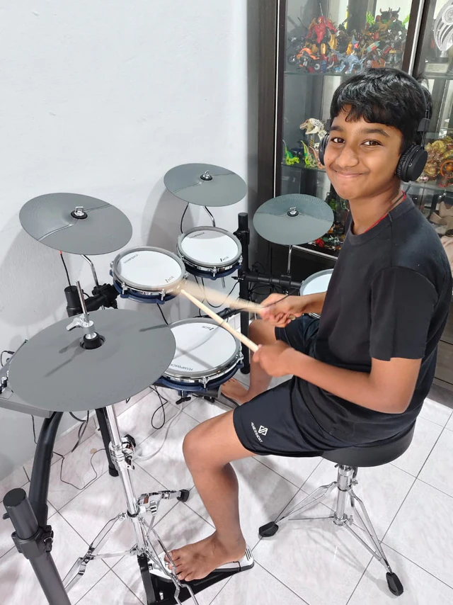 Young drummer playing an electronic drum kit with headphones at home in Malaysia