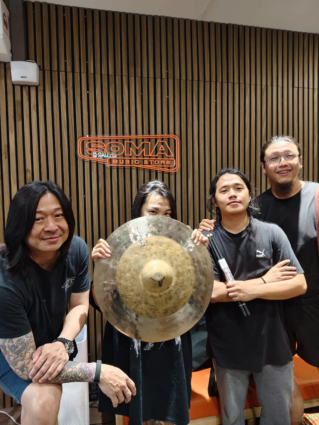 A group of customers with a cymbal and drumsticks beneath the Soma Music sign
