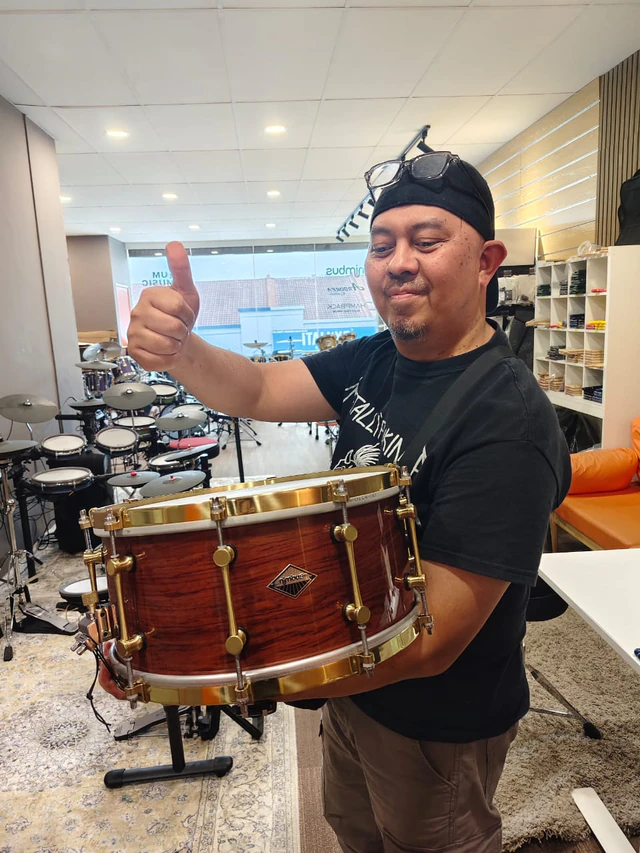Customer holding a wood-finish snare drum with gold-coloured hardware